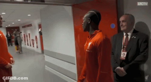 A Man In A Suit Stands Next To A Man In A Red Shirt That Says Lfc Tv GIF