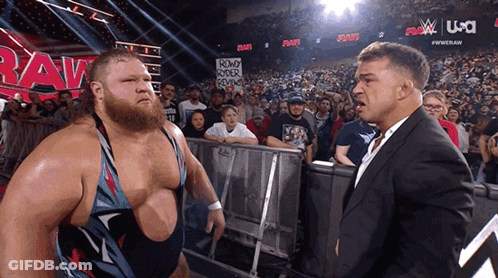 A Man In A Suit Stands Next To A Man In A Wrestling Ring With A Sign That Says Round Rock Reviews GIF