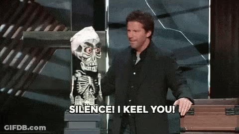 A Man In A Suit Stands Next To A Skeleton Puppet And Says Silence I Keel You GIF