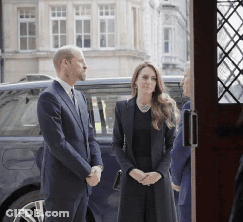 A Man In A Suit Stands Next To A Woman In A Black Dress GIF