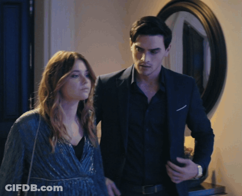 A Man In A Suit Stands Next To A Woman In A Blue Dress GIF
