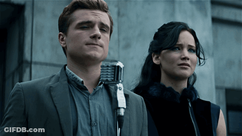 A Man In A Suit Stands Next To A Woman In A Fur Coat GIF