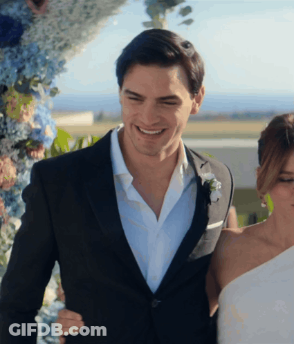 A Man In A Suit Stands Next To A Woman In A Wedding Dress GIF