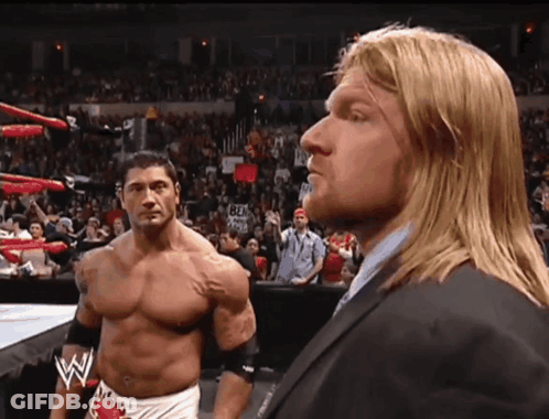 A Man In A Suit Stands Next To Another Man In A Wrestling Ring GIF