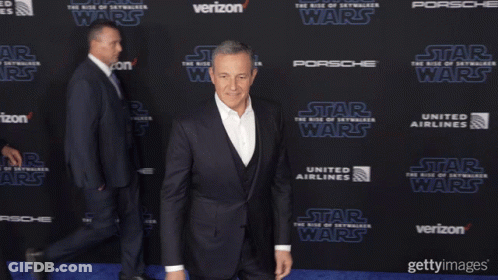 A Man In A Suit Stands On A Blue Carpet With The Word Star Wars On It GIF