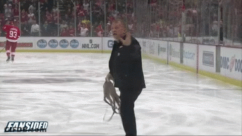A Man In A Suit Stands On A Hockey Rink In Front Of An Nhl.com Sign GIF