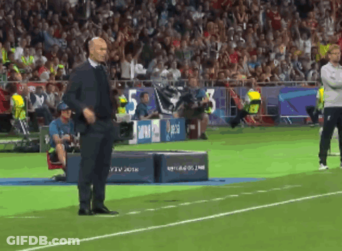 A Man In A Suit Stands On A Soccer Field In Front Of A Banner That Says 5 GIF