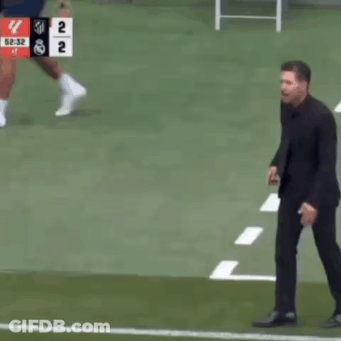 A Man In A Suit Stands On A Soccer Field With A Scoreboard Behind Him That Says 2 To 1 GIF