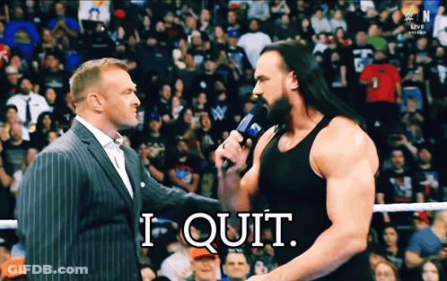 A Man In A Suit Talks Into A Microphone While Another Man Says " I Quit " In Front Of A Crowd GIF