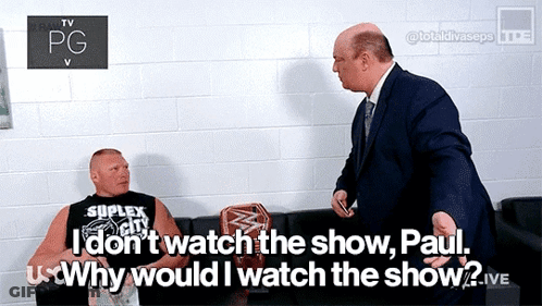 A Man In A Suit Talks To A Man In A Black Shirt That Says Suplex City GIF