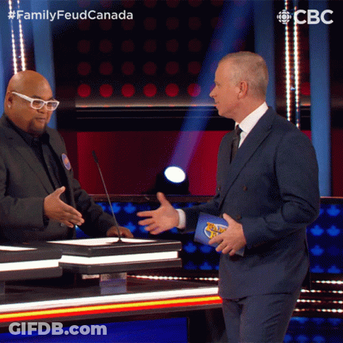 A Man In A Suit Talks To Another Man On A Stage With A Cbs Logo In The Background GIF