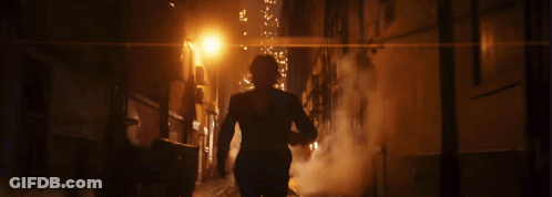 A Man In A Suit Walks Down A Dark Alley At Night GIF