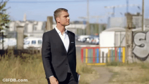 A Man In A Suit Walks In Front Of Graffiti That Says ' S ' On It GIF