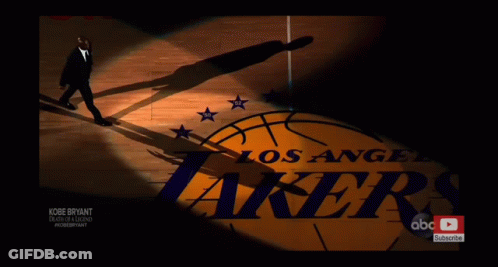 A Man In A Suit Walks On A Basketball Court With The Los Angeles Lakers Logo In The Background GIF
