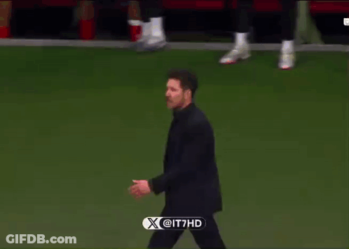 A Man In A Suit Walks On A Soccer Field With A X @ It7hd Logo In The Corner GIF