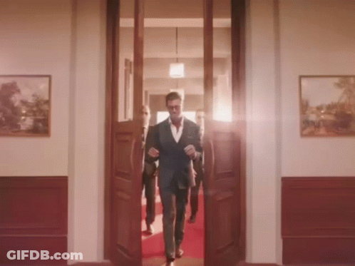 A Man In A Suit Walks Through A Doorway GIF