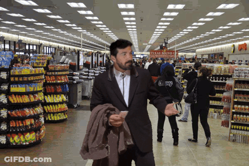 A Man In A Suit Walks Through A Grocery Store With A Sign That Says Texas Roundup GIF