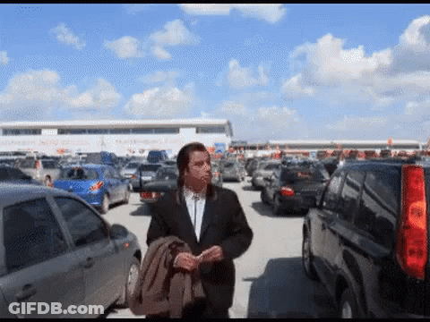A Man In A Suit Walks Through A Parking Lot GIF