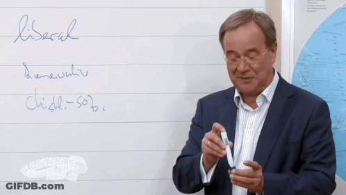 A Man In A Suit Waves In Front Of A Whiteboard That Has The Word Lisbach Written On It GIF