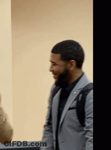 A Man In A Suit With A Backpack On His Back Is Smiling GIF