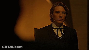 A Man In A Suit With A Bow Tie Is Standing In A Dark Room GIF