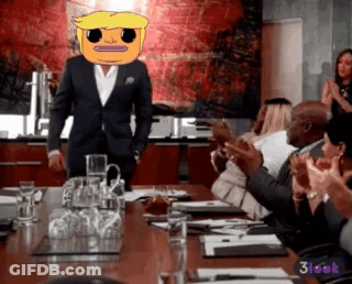 A Man In A Suit With A Cartoon Face On His Head Stands In Front Of A Group Of People Clapping GIF