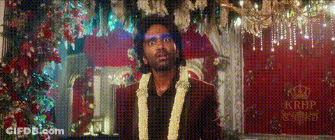 A Man In A Suit With A Garland Around His Neck Is Standing In Front Of A Red Curtain . GIF