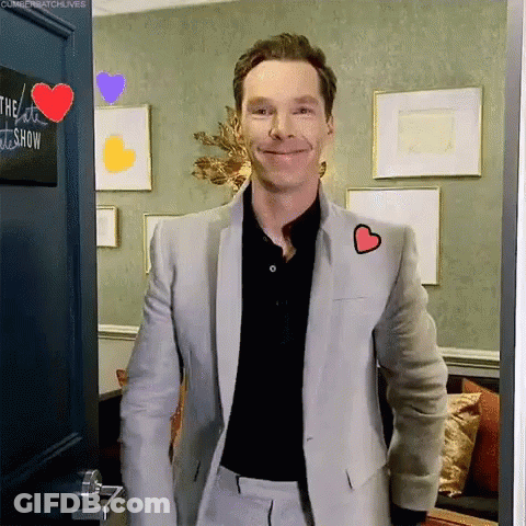 A Man In A Suit With A Heart On His Jacket Is Standing In A Doorway . GIF