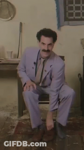 A Man In A Suit With A Mustache Is Squatting Down GIF
