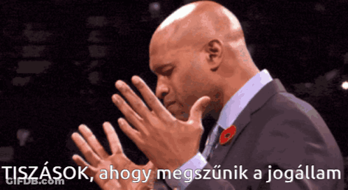 A Man In A Suit With A Poppy On His Lapel Holds His Hands Together In Prayer GIF