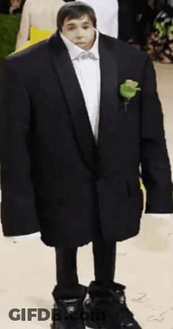 A Man In A Suit With A Rose In His Pocket Is Standing On A Carpet GIF