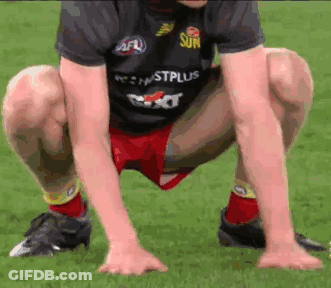 A Man In A Sun Shirt Squatting Down On The Grass GIF