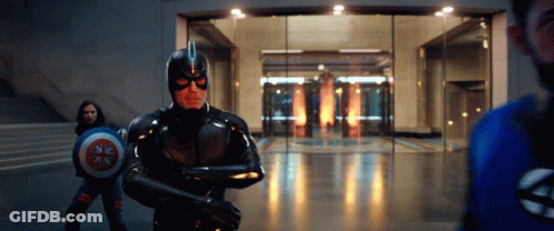 A Man In A Superhero Costume Is Holding A Shield In Front Of A Glass Door . GIF