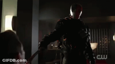 A Man In A Superhero Costume Is Holding A Sword In His Hand In A Dark Room . GIF