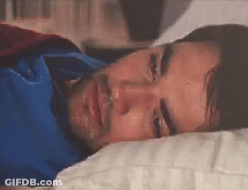 A Man In A Superhero Costume Is Laying In A Bed With His Eyes Closed . GIF