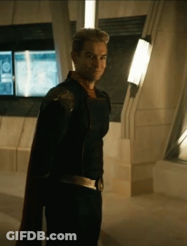 A Man In A Superhero Costume Is Standing In A Room With A Cape . GIF