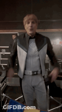 A Man In A Superhero Costume Is Standing In Front Of A Chair With A Blue And Yellow Flag GIF