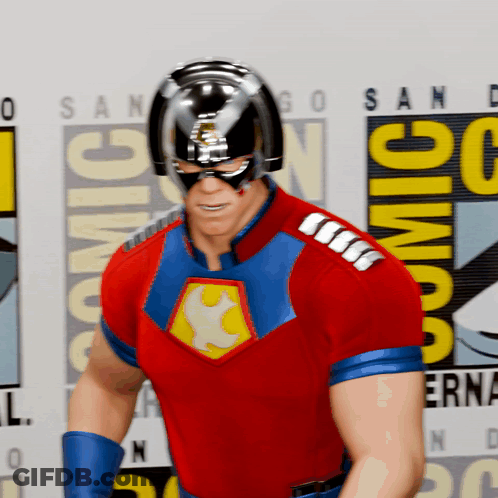 A Man In A Superhero Costume Is Standing In Front Of A Comic Con Logo GIF