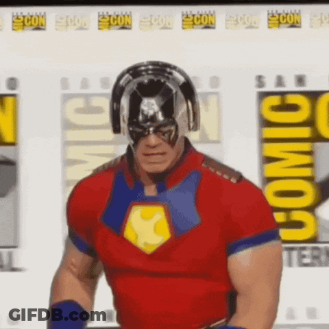 A Man In A Superhero Costume Is Standing In Front Of A Comic Con Poster . GIF