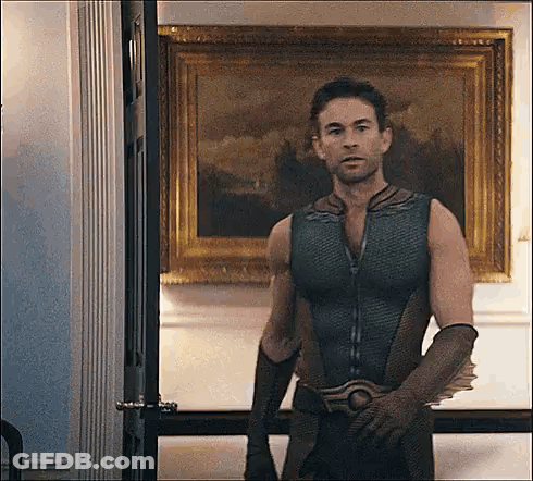 A Man In A Superhero Costume Is Standing In Front Of A Painting In A Room . GIF