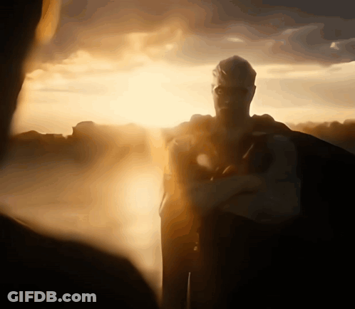 A Man In A Superhero Costume Stands In Front Of The Sun GIF