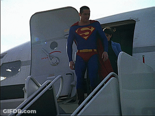A Man In A Superman Costume Climbs The Stairs Of An Airplane GIF