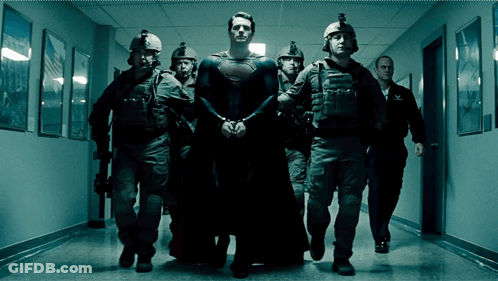 A Man In A Superman Costume Is Being Escorted Down A Hallway By Police Officers GIF