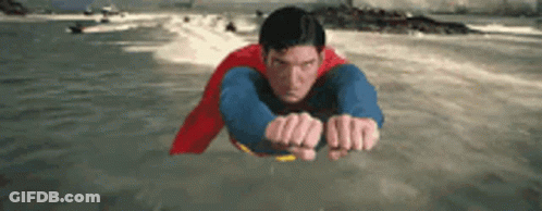 A Man In A Superman Costume Is Flying Over The Water . GIF