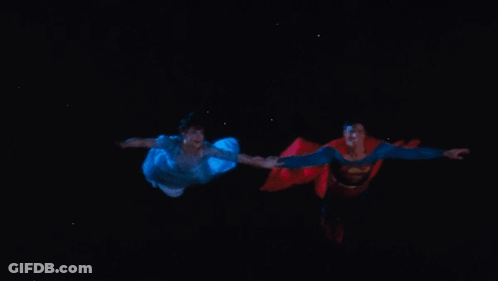 A Man In A Superman Costume Is Holding A Woman 'S Hand GIF