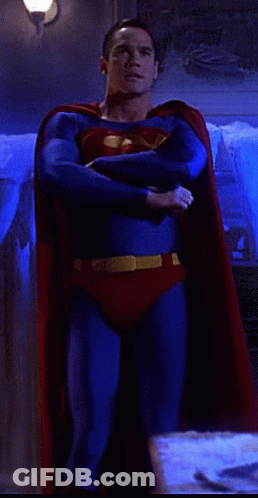 A Man In A Superman Costume Is Standing In A Room With His Arms Crossed GIF
