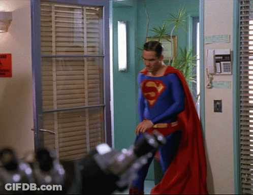 A Man In A Superman Costume Is Standing In Front Of A Door GIF