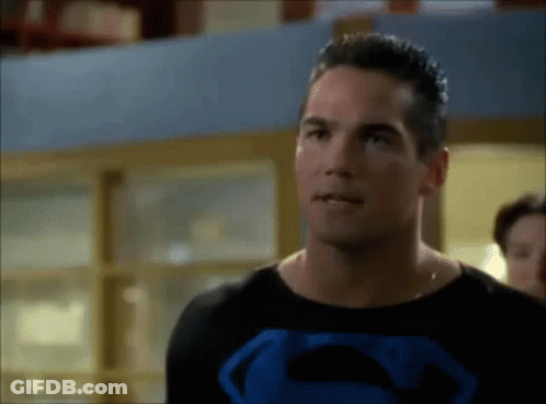 A Man In A Superman Costume Is Standing In Front Of A Window . GIF