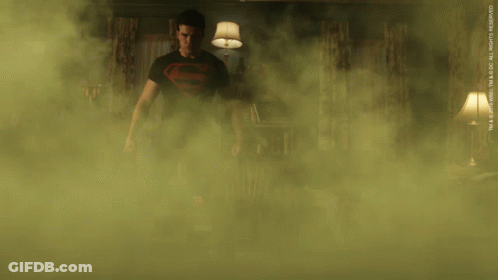 A Man In A Superman Shirt Is Standing In A Room Surrounded By Smoke GIF