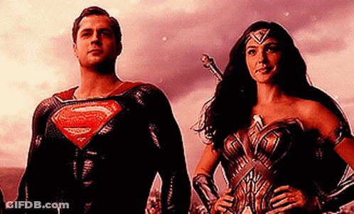 A Man In A Superman Suit And A Woman In A Wonder Woman Outfit Are Standing Next To Each Other . GIF